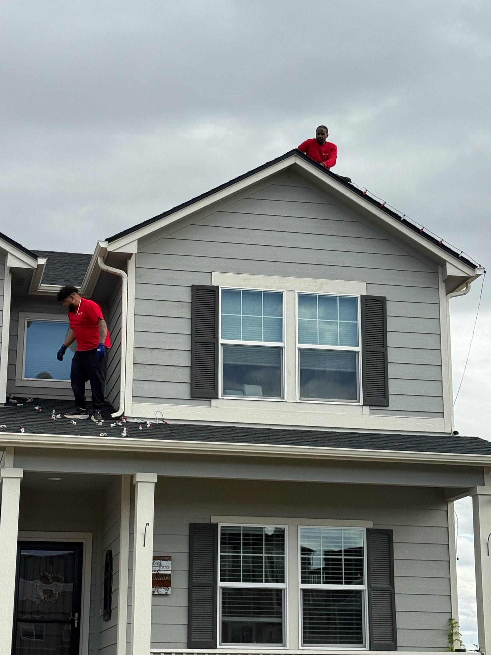 Our installers on roof peak hanging holiday lights on a gray Front Range house Our installers on roof peak hanging holiday lights on a gray Front Range house